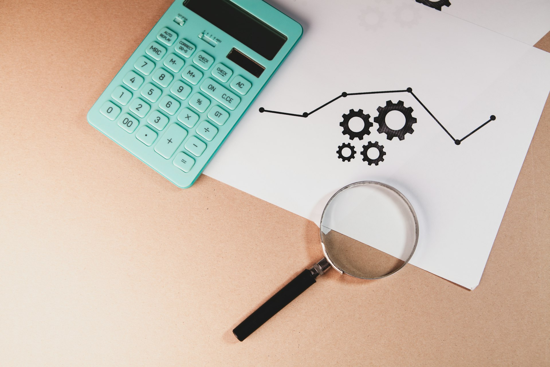 Calculator, magnifying glass, and chart with gears on paper.